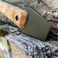 A close-up of a hand axe or hatchet with a natural wood handle and an olive green metal blade, resting against a weathered wooden surface outdoors.